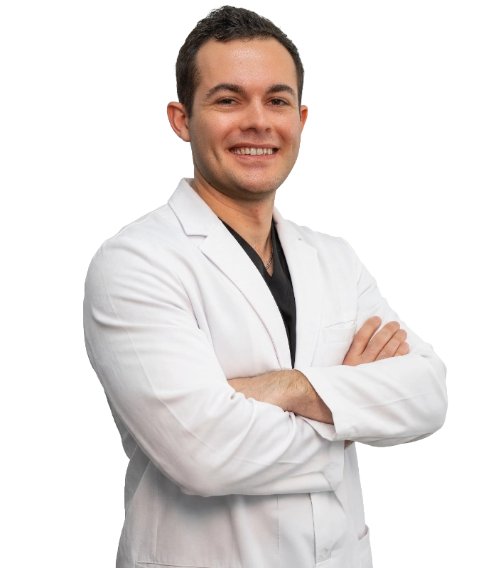 This is a professional headshot of Dr. Kyle Mele wearing a white lab coat over a black scrub top. He is smiling and posing with his arms crossed against a plain black background.